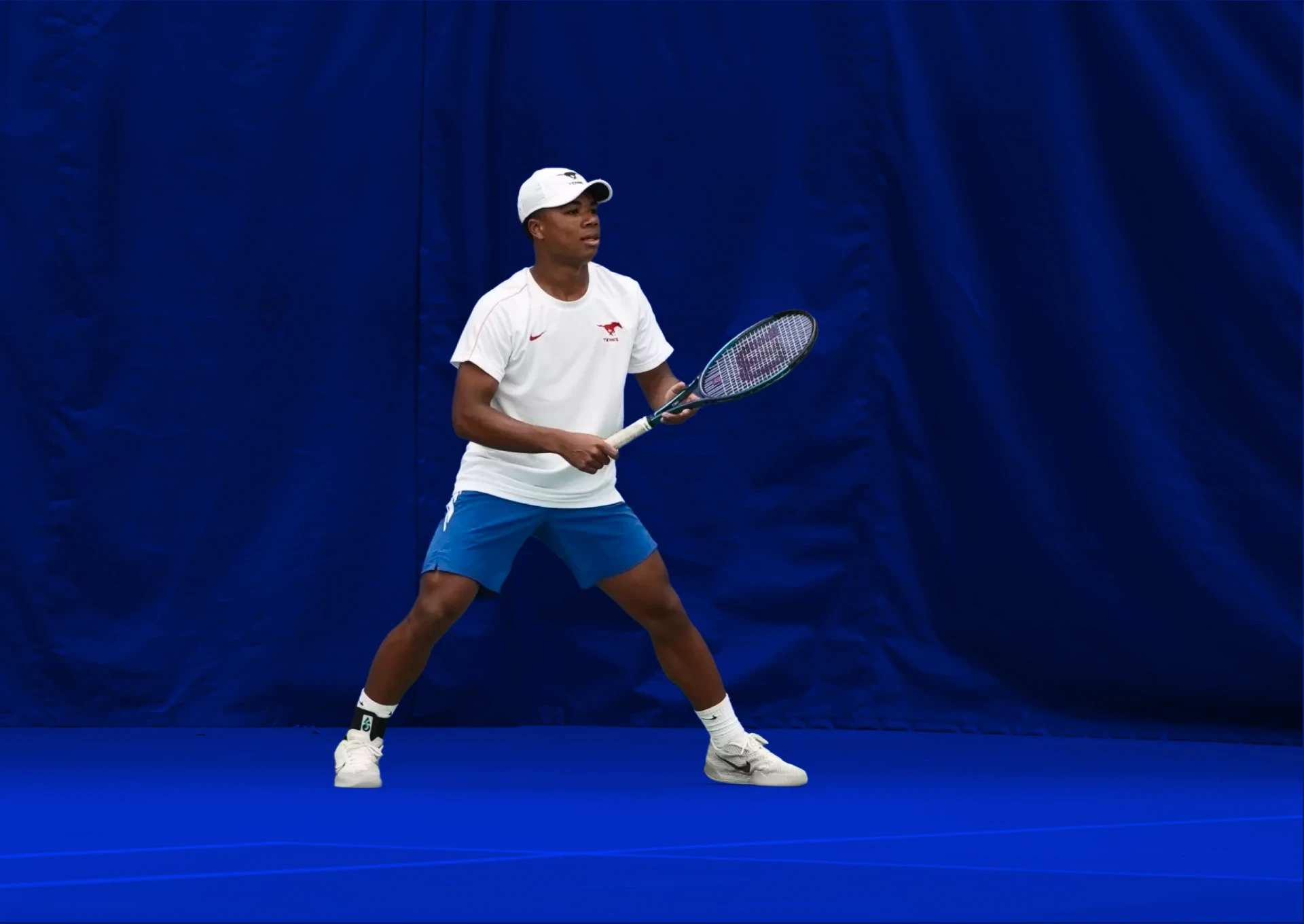 SMU tennis student-athlete ready to return a serve in front of the SMU Mustangs banner