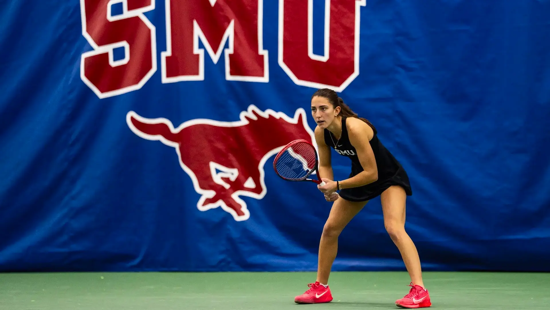SMU tennis student-athlete ready to return a serve in front of the SMU Mustangs banner